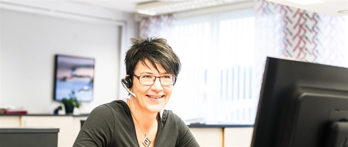 Alt=smilende dame sittende foran en PC-skjerm